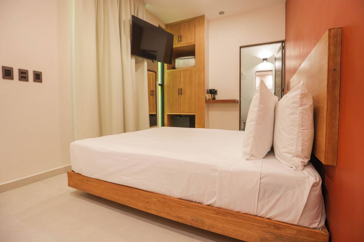 Una camera d'albergo moderna con un letto a telaio di legno, biancheria bianca, una TV a schermo piatto montata a parete e un armadio in legno.