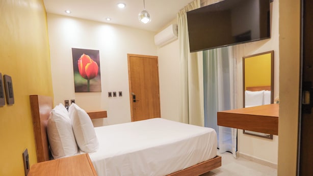 Ein Hotelzimmer mit einem Bett, einem Nachttisch aus Holz, einem Spiegel, einem Fernseher und einem Blumenbild an der Wand.