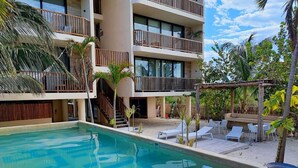 A pool area with a clear blue pool, lounge chairs, and a building with balconies. - BOHO Loft Steps from the Beach (Holbox)