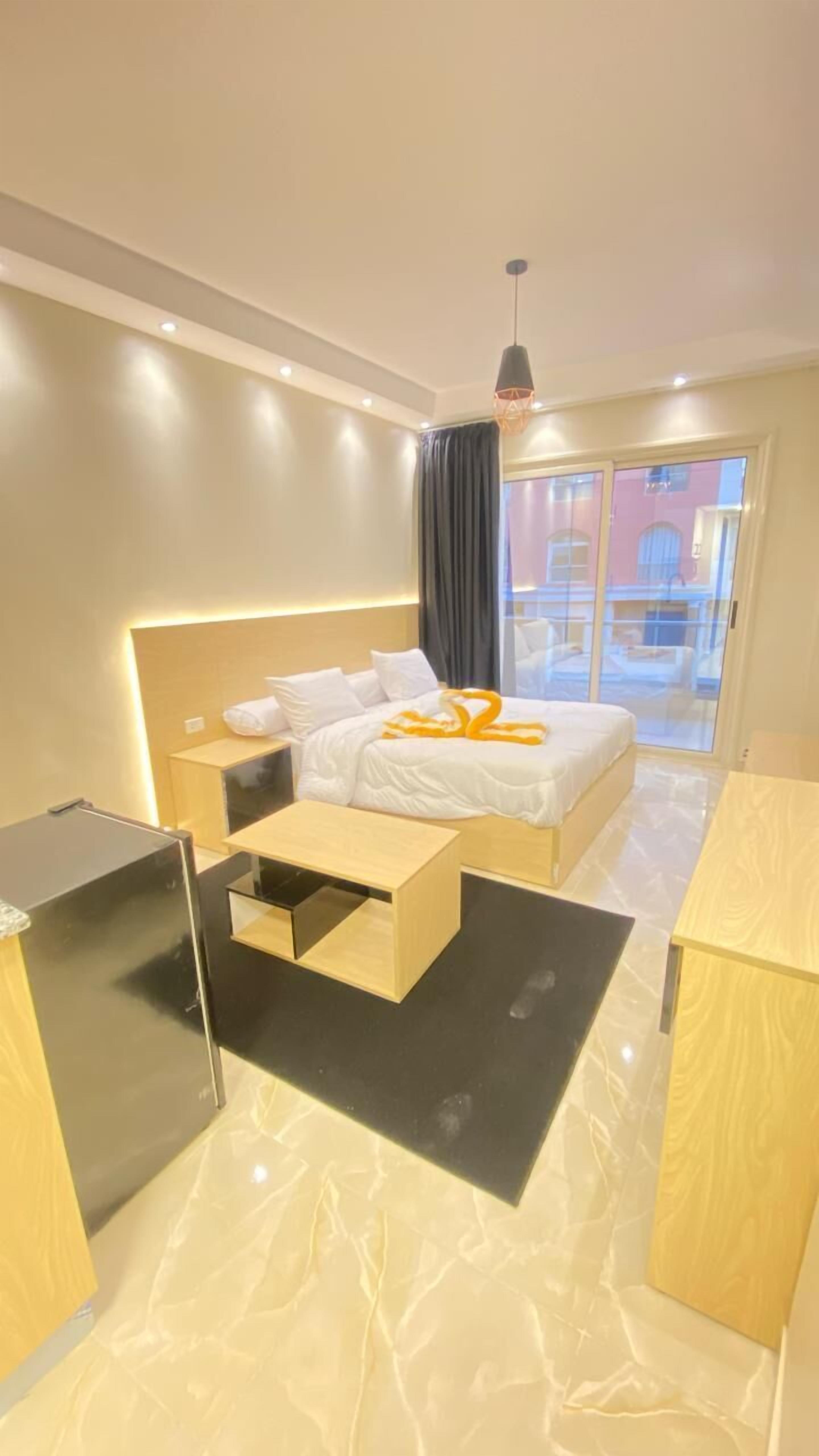 A modern hotel room with a bed, bedside tables, a desk, and a large window with a view.