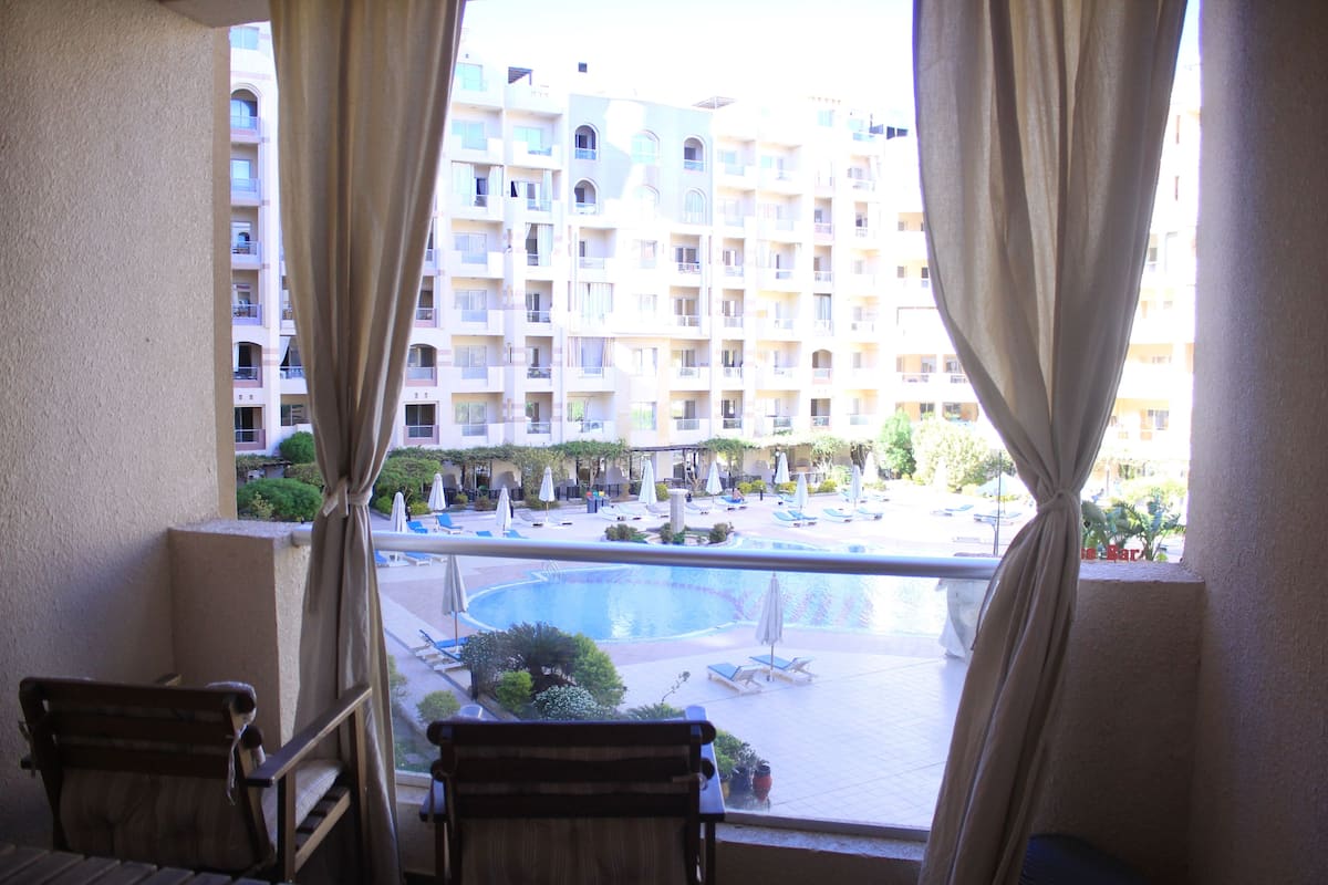 A balcony with a view of a swimming pool and a multi-story building in the background.