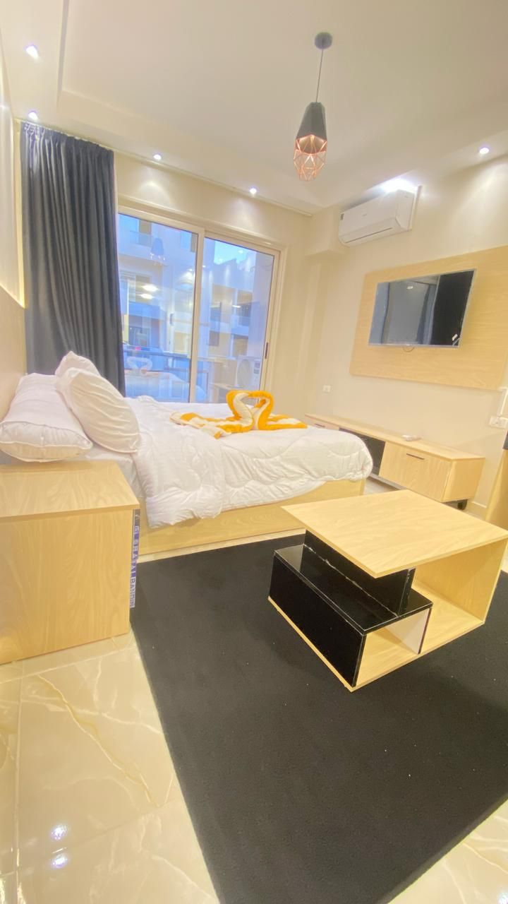 Une chambre d’hôtel comprenant un lit, un bureau, une chaise, un meuble de rangement noir, une fenêtre avec des rideaux et un luminaire au plafond.