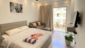 A modern hotel room with a large bed, a sofa, a TV, and a balcony with a view. - Florenza Khamsin Resort (Hurghada)