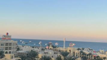 Un pueblo costero con edificios que presentan ventanas arqueadas y balcones, una torre destacada y vista al mar con barcos.