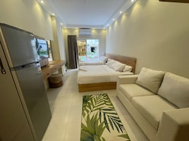 A modern hotel room with a bed, a sofa, a desk, and a refrigerator.