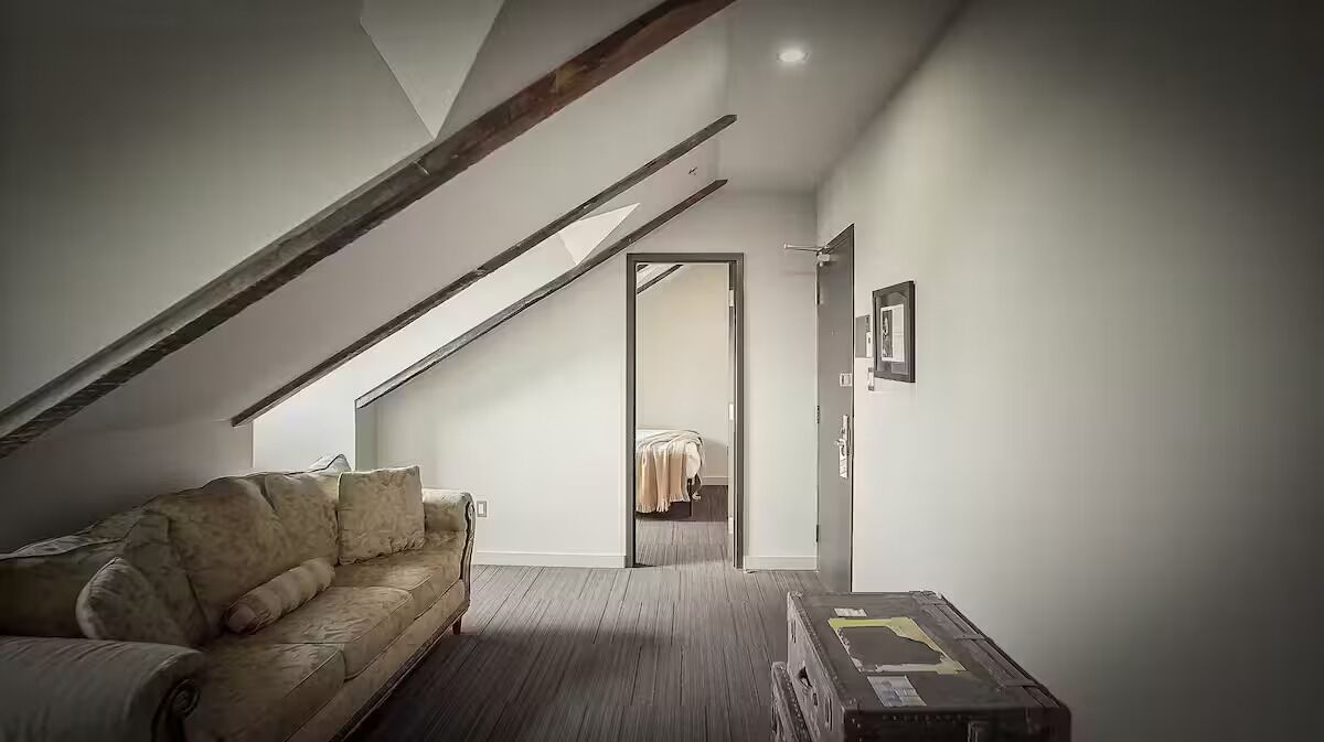 Una habitación estilo loft con techo inclinado, un sofá, una mesita y una puerta que da a otra habitación.