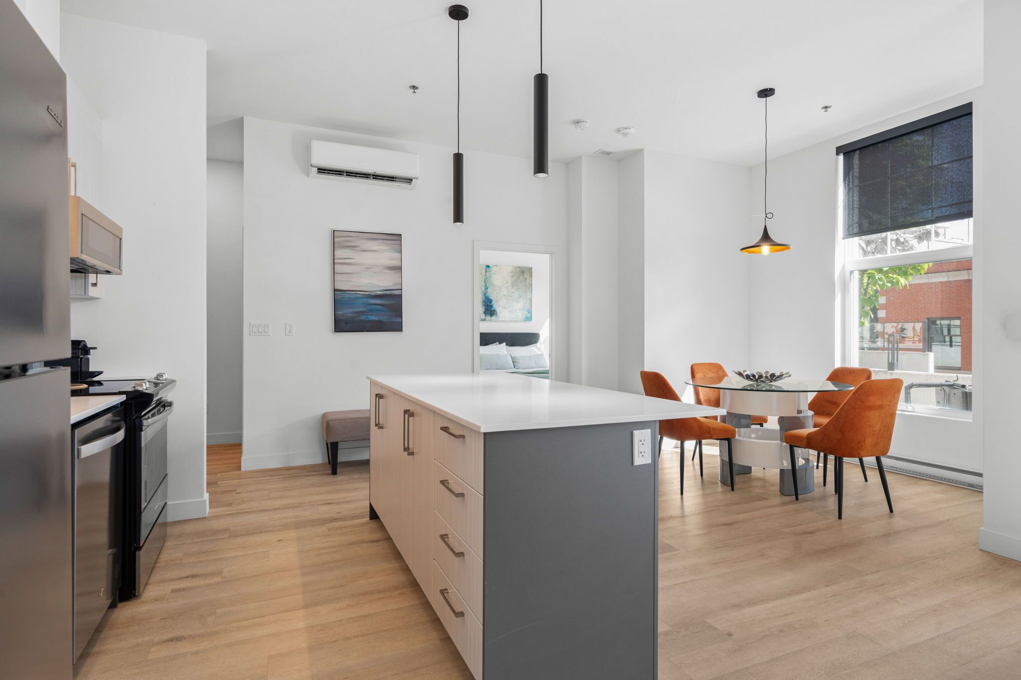 Una cocina moderna con una isla central, un comedor con sillas color naranja y un amplio ventanal con vistas al exterior.