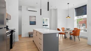 Una cocina moderna con una isla central, un comedor con sillas color naranja y un amplio ventanal con vistas al exterior.