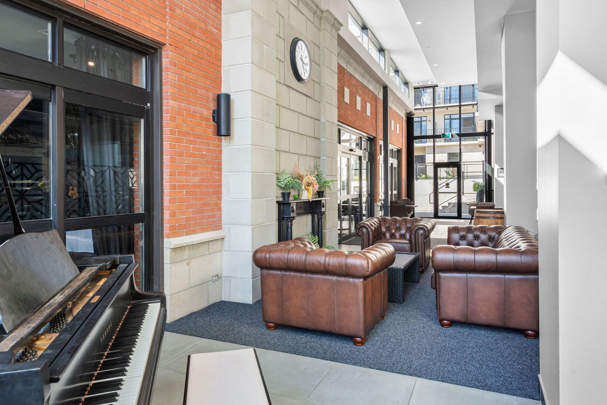 A lobby with a grand piano, leather sofas, a clock, and a view of the building's exterior.