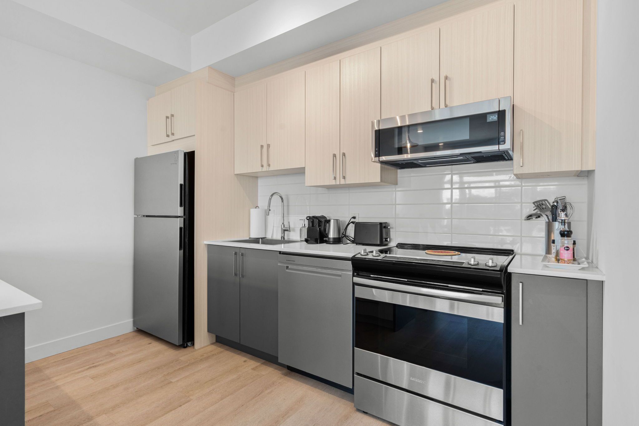A modern kitchen with stainless steel appliances, light wood cabinets, and a white tiled backsplash.