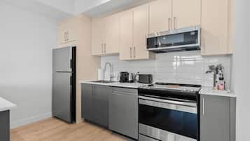 Una cocina moderna con electrodomésticos de acero inoxidable, armarios de madera clara y salpicadero de azulejos blancos.