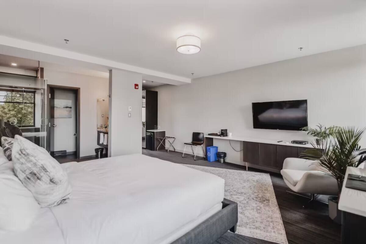 A modern hotel room with a large bed, a TV, a desk, and a seating area.