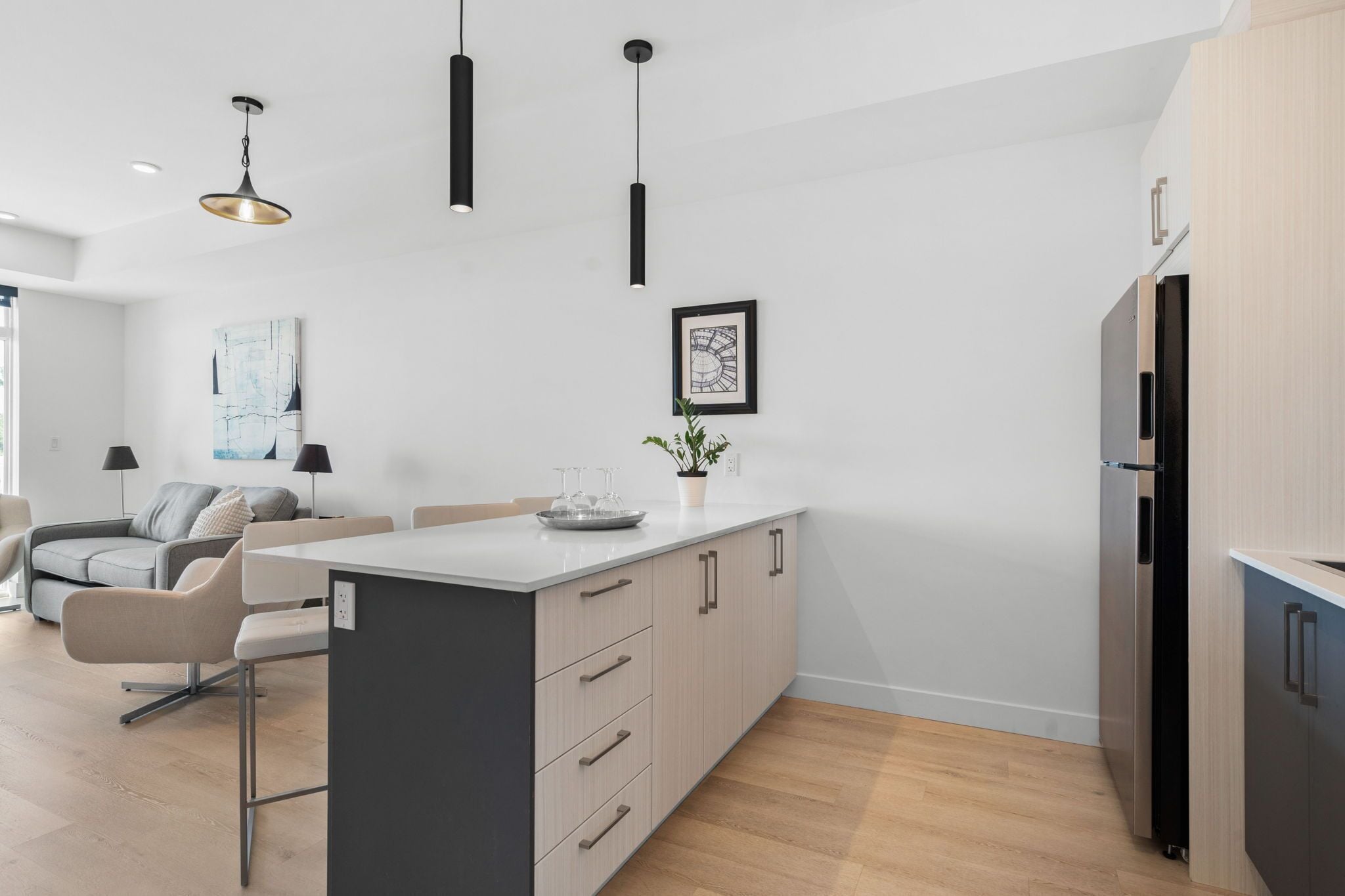 A modern kitchen with a central island, pendant lighting, and a refrigerator.