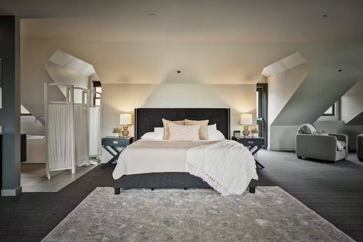 A modern bedroom with a large bed, bedside tables, a chair, and a view of the outside.