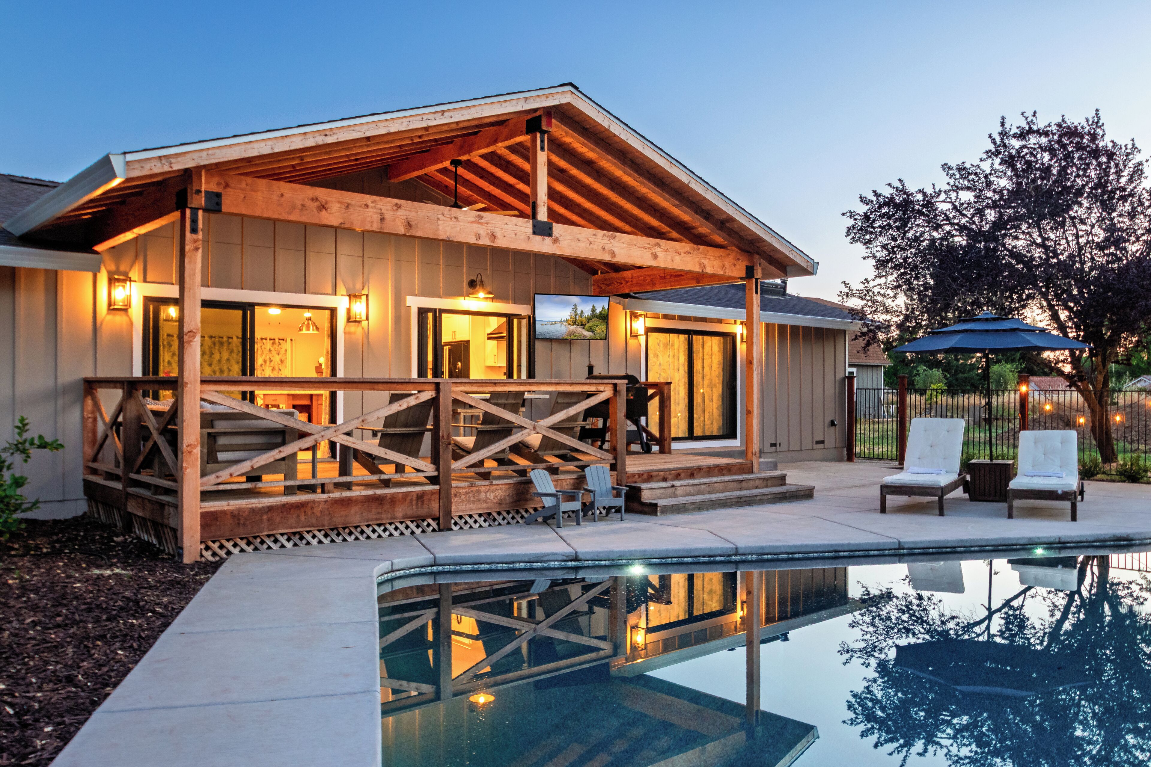 Ein Holzhaus mit überdachter Terrasse, Schwimmbad und Gartenmöbeln.