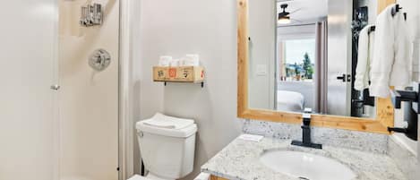 A modern bathroom with a glass-enclosed shower, a toilet, a sink with a granite countertop, and a wooden-framed mirror.
