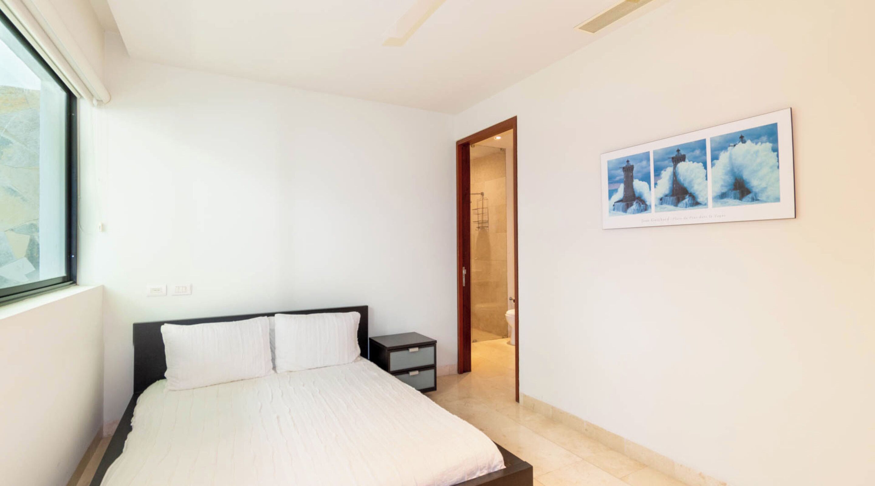 Ein Schlafzimmer mit Bett, Nachttisch, Fenster und einer Tür zum Badezimmer.