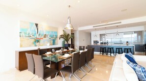 A modern kitchen with a central island, bar stools, and a dining area with a glass table and chairs. - Cruz de Huanacaxtle Arena Blanca 408 (La Cruz de Huanacaxtle)