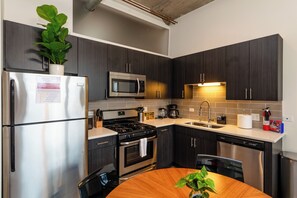 Une cuisine moderne dotée d’appareils électroménagers en acier inoxydable, de meubles de rangement aux couleurs sombres et d’une table à manger en bois.