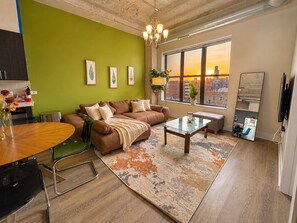 Un salon moderne avec un mur d’accent vert, un canapé, une table basse et une grande fenêtre donnant sur la ville.