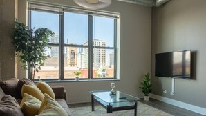 Un salon moderne avec une grande fenêtre, un canapé, une table basse et un téléviseur fixé au mur.