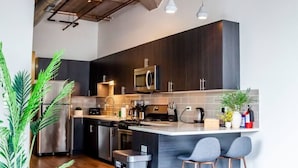 A modern kitchen with dark wood cabinets, stainless steel appliances, and a central island with bar stools. - Modern 3BR Corner Suite Near McCormick Place & Soldier Field that Sleeps 10 (Chicago)