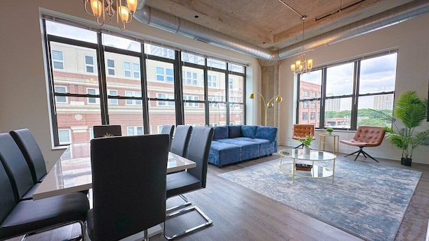 A modern office space with a large table, several chairs, a blue sofa, and a coffee table. - Modern 3BR Corner Suite Near McCormick Place & Soldier Field that Sleeps 10 (Chicago)