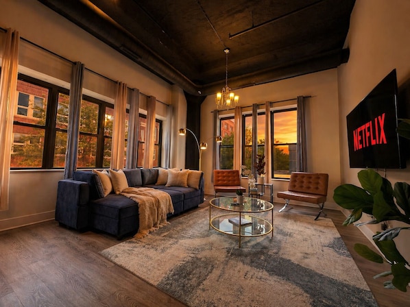 A modern living room with a sectional sofa, a glass coffee table, and a large TV displaying the Netflix logo.
