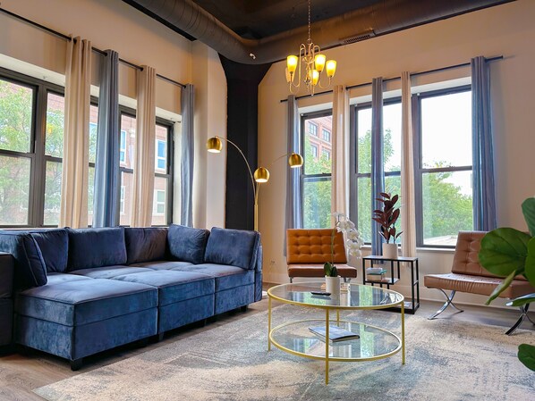 Una sala moderna con un sofá azul, una mesa de centro redonda de cristal y un sillón marrón.