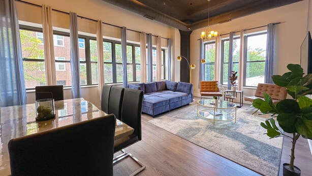 Een ruime woonkamer met een blauwe bank, een ronde glazen salontafel en een eettafel met stoelen.