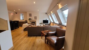 A modern living room with a sectional sofa, a leather armchair, a wooden coffee table, and a flat-screen TV. There is a fireplace and a skylight above the TV. - Spacious 3BR apartment with rooftop terrace (Antwerpen)