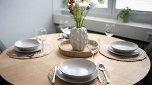 Ein runder Esstisch mit drei weißen Tellern, zwei Weingläsern und einer Blumenvase.
