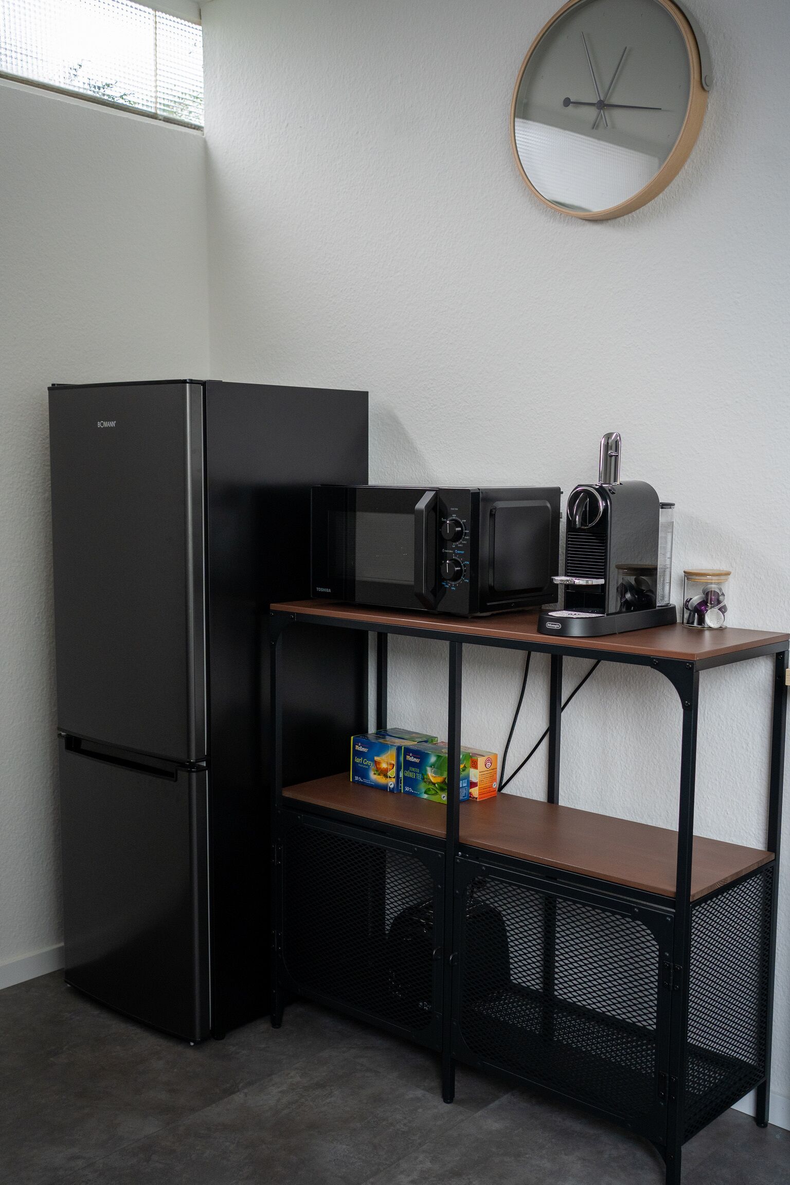 A compact kitchenette with a black refrigerator, a microwave, a toaster, and a coffee maker on a wooden table.