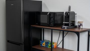 A compact kitchenette with a black refrigerator, a microwave, a toaster, and a coffee maker on a wooden table.