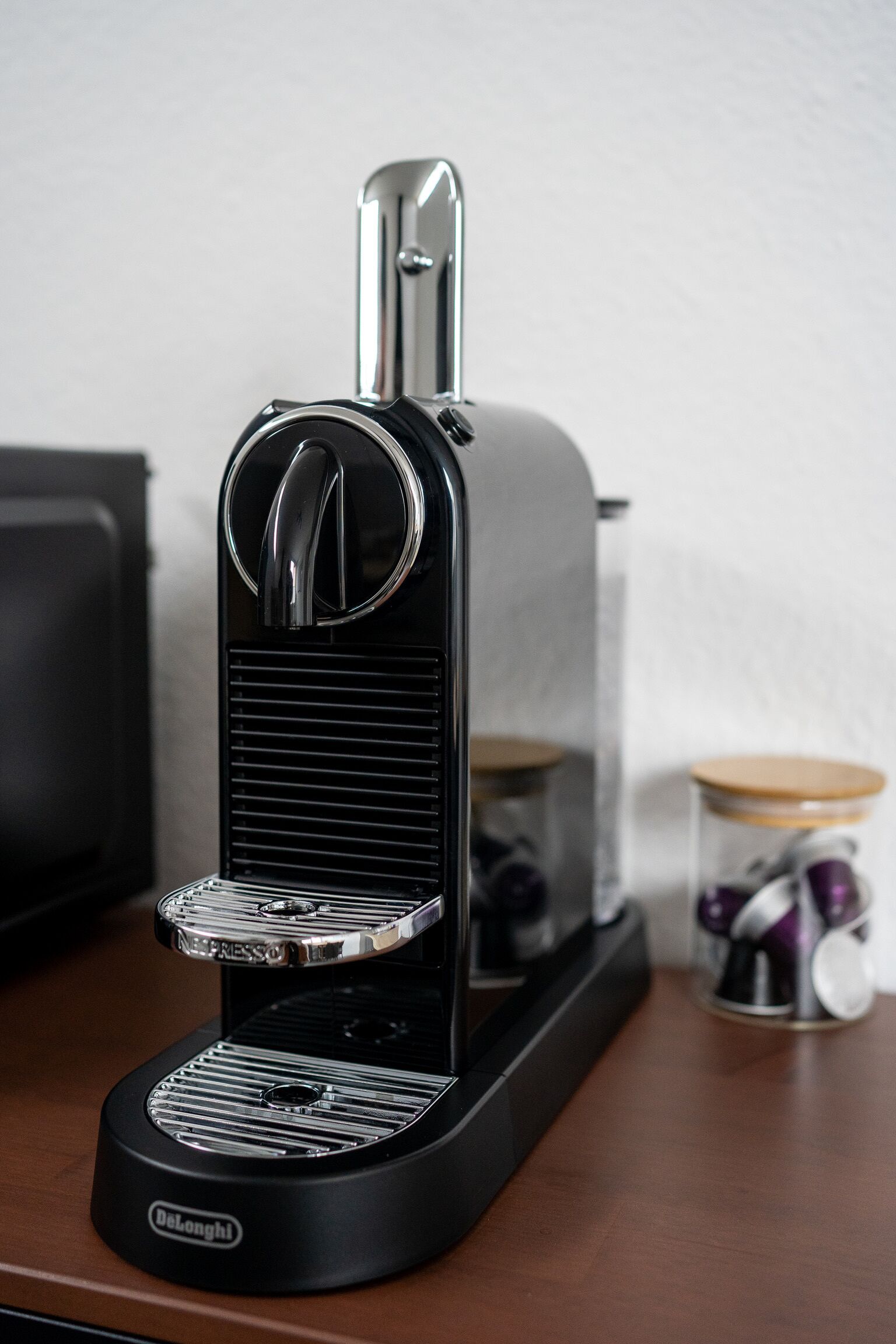 A De'Longhi espresso machine on a wooden table with a jar of pasta and a black appliance in the background.