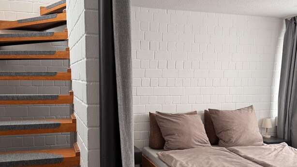 Ein modernes Schlafzimmer mit weißer Ziegelwand, einem Holzbettgestell und einem grauen Vorhang.