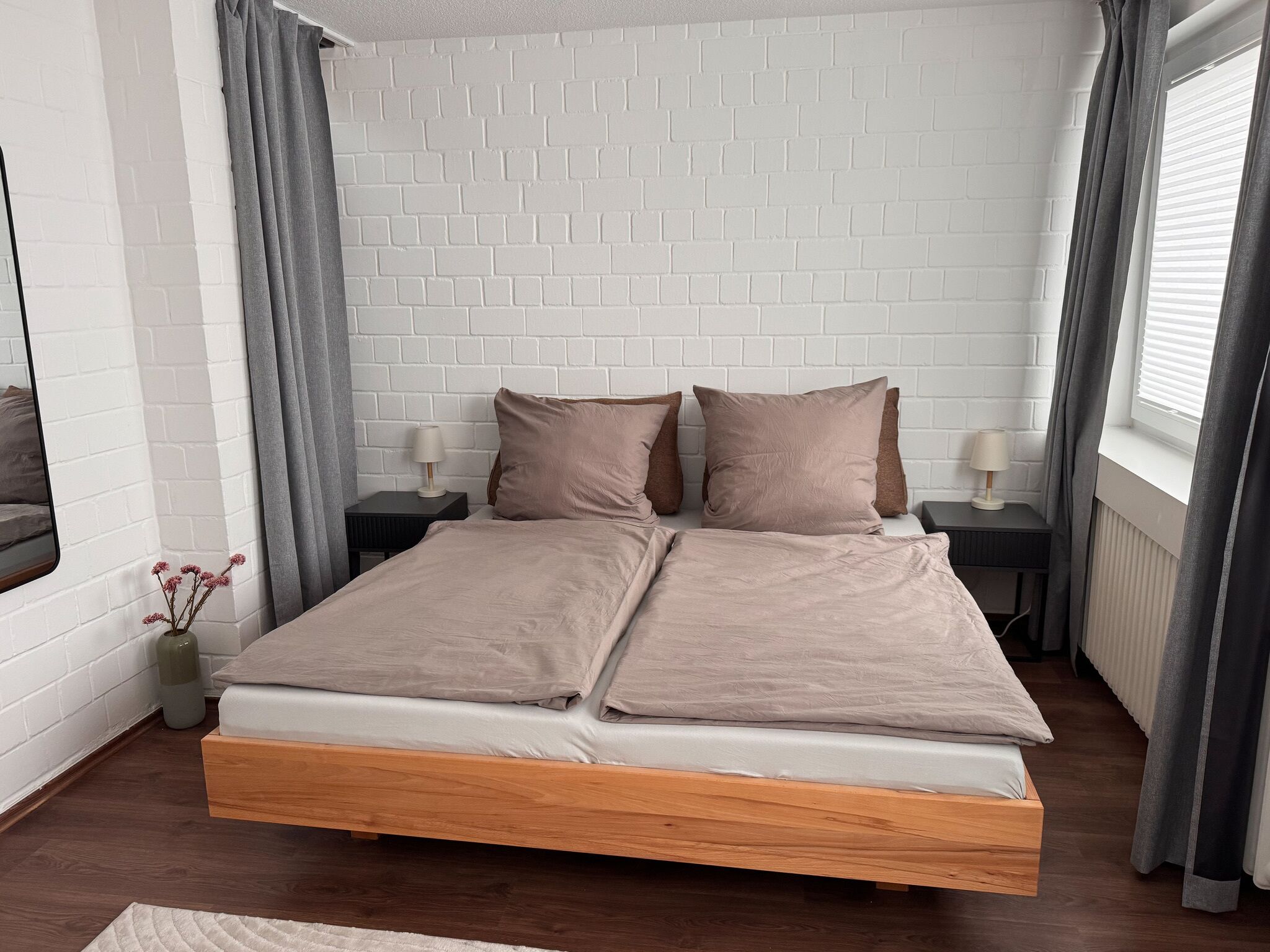 A modern bedroom with a white brick wall, a wooden bed frame, and two bedside tables with lamps.