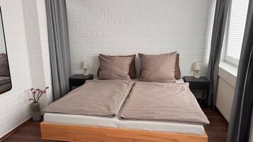 A modern bedroom with a white brick wall, a wooden bed frame, and two bedside tables with lamps.
