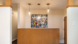 Un'area reception con un bancone in legno, un'opera d'arte colorata al muro e tre lampade a sospensione.