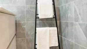 A bathroom with a black metal towel rack holding two white towels against a tiled wall. - Dimora Cinque Santi (Naples)