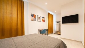 A hotel room with a bed, a desk, a chair, a TV, and artwork on the wall. - Dimora Cinque Santi (Naples)