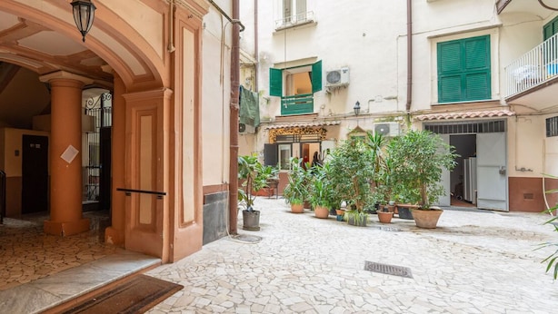 A narrow cobblestone street with a building entrance featuring a wooden door and an arched doorway. - Dimora Cinque Santi (Naples)