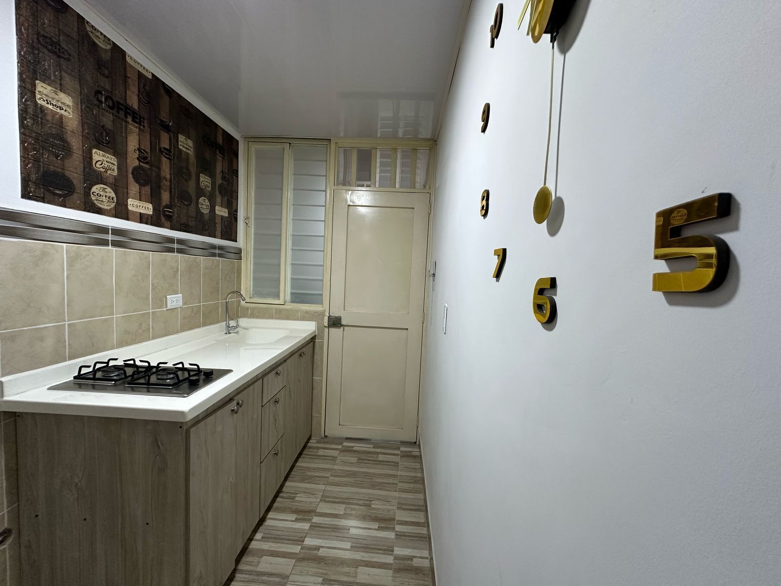 A narrow kitchen with a white countertop, a gas stove, and a tiled backsplash with coffee-themed decorations.