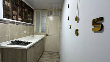 A narrow kitchen with a white countertop, a gas stove, and a tiled backsplash with coffee-themed decorations.