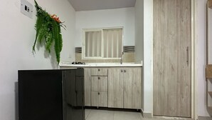 Μια μικρή κουζίνα με ένα μαύρο ψυγείο, ξύλινα ντουλάπια, ένα παράθυρο και μια πόρτα.