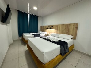A hotel room with two beds, a wooden headboard, a flat-screen TV, and a ceiling light. - Hospedarte Cali (Cali)