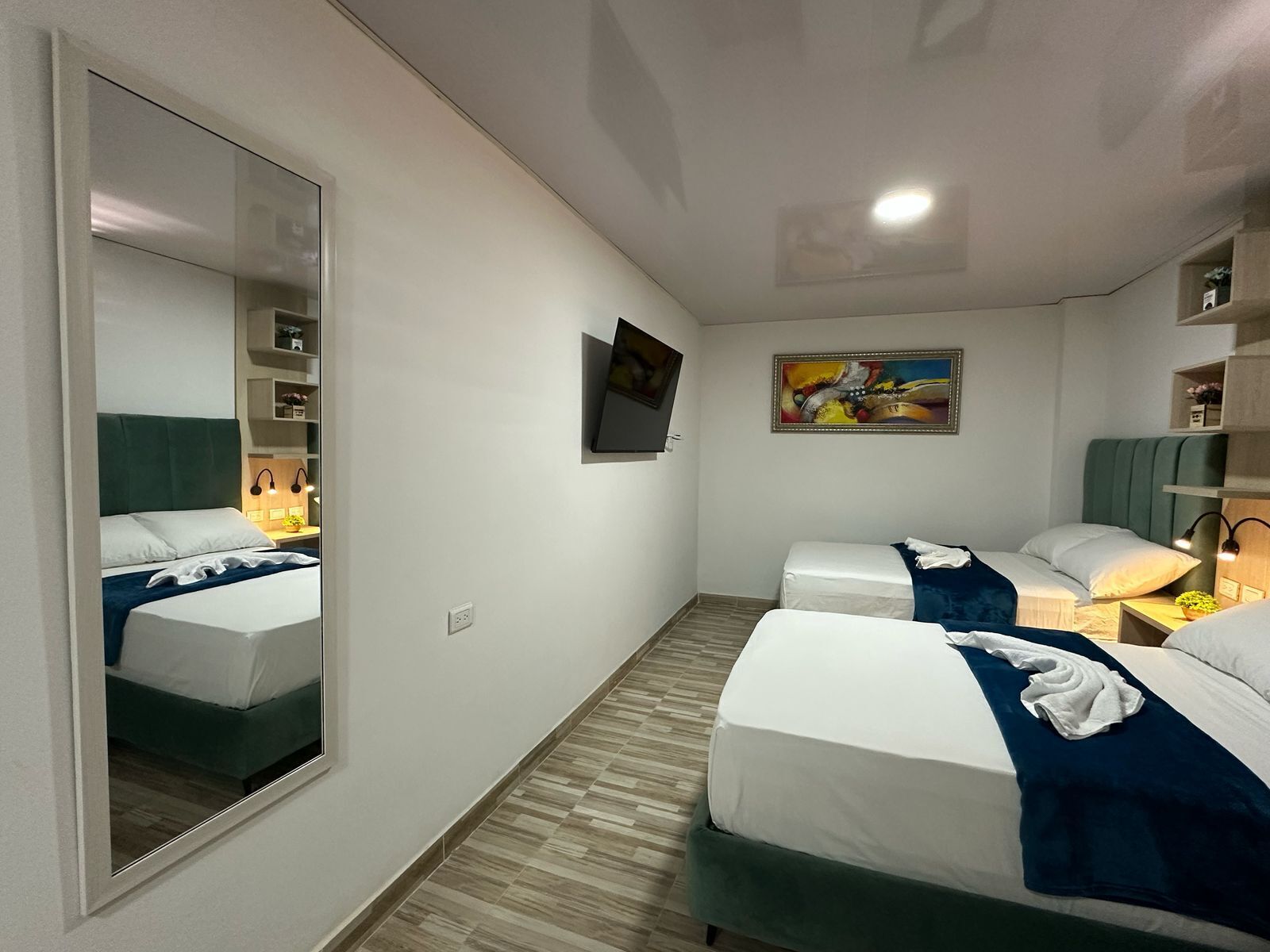 A hotel room with two beds, a large mirror, a painting, and a TV on the wall.