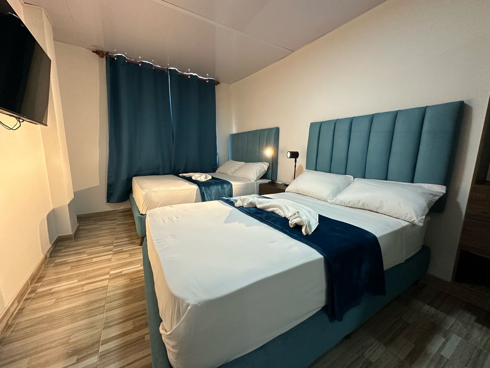 A hotel room with two beds, a TV, and a nightstand with a lamp.