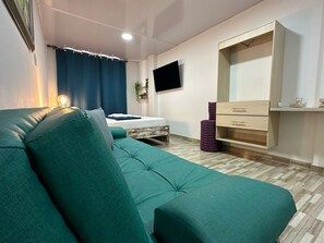 A modern room with a teal sofa, a bed with a blue curtain, a TV mounted on the wall, and a wooden wardrobe. - Hospedarte Cali (Cali)