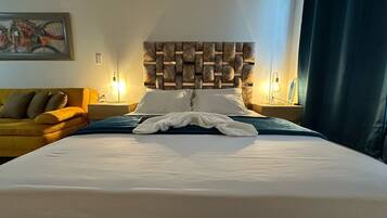 A hotel room with a large bed, a wooden headboard, a yellow sofa, and two bedside lamps.